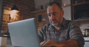 A confused middle-aged man is looking at his laptop screen